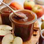 A jar of apple butter with a spoon being dipped into it.