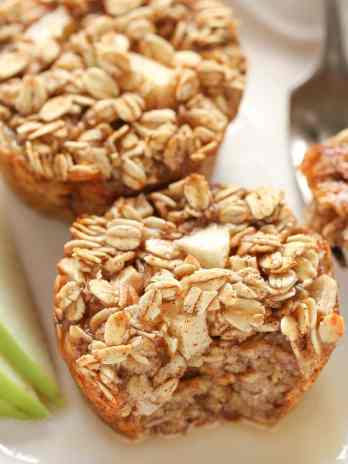 Two apple cinnamon baked oatmeal cups on a white plate with a fork and apple slices.