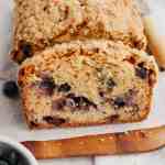 A loaf of blueberry bread that's been sliced on a wooden cutting board.