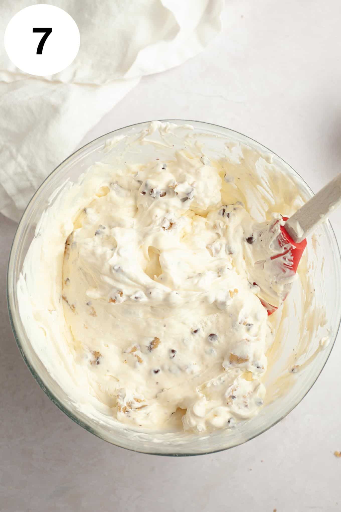 An overhead view of chocolate chip cookie dough ice cream in a glass mixing bowl, with a rubber spatula. 