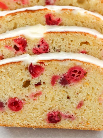A loaf of cranberry orange bread sliced up on a piece of parchment paper.
