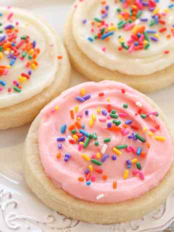 Three frosted sugar cookies on a white plate topped with sprinkles.
