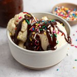 A bowl of ice cream topped with hot fudge sauce and sprinkles.