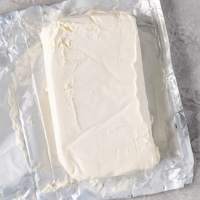 A block of cream cheese that's been opened and is sitting on the wrapper.