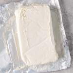 A block of cream cheese that's been opened and is sitting on the wrapper.