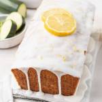 A loaf of lemon zucchini bread topped with two lemon slices. Some sliced zucchini rests in a small bowl on the side.