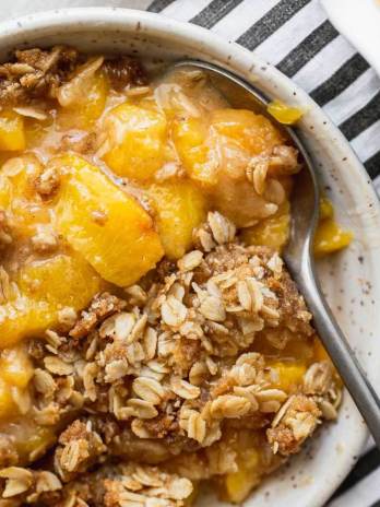 A bowl of peach crisp with a spoon in it.