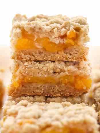 A stack of peach crumble bars, with additional bars surrounding the stack.