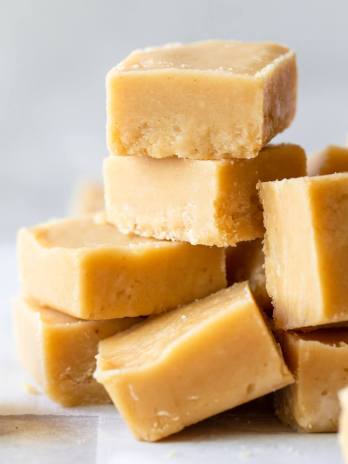 Pieces of Peanut Butter Fudge stacked on a gray surface and parchment paper.