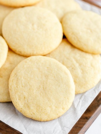 A decorative wood board covered with a stack of sugar cookies.
