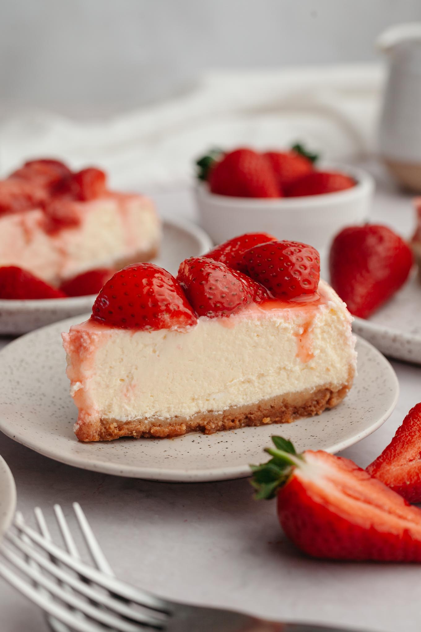 A slice of cheesecake with strawberry topping on a white plate. 
