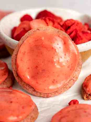 A strawberry cookie leaning on a bowl of freeze-dried strawberries.